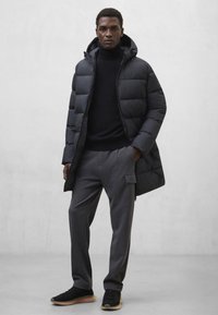 Czarna pikowana kurtka z kapturem, noszona na czarnym swetrze. Szare spodnie cargo z bocznymi kieszeniami i czarne sneakersy z gumowymi podeszwami.