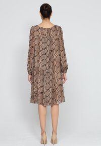 Brązowa sukienka w wzór wężowy z długimi rękawami, luźnym krojem, okrągłym dekoltem i marszczonymi mankietami, wykonana z lekkiego materiału.