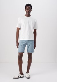 Hvid kortærmet t-shirt, lyseblå rullede shorts, og hvide sneakers med sorte detaljer. Simpelt design, bomuldsstof, afslappet pasform.