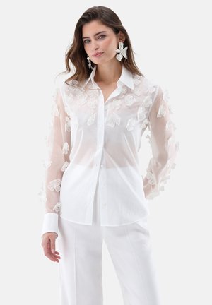 White sheer button-up shirt with embroidered white flower accents on sleeves. Features classic collar and long sleeves. Smooth texture.