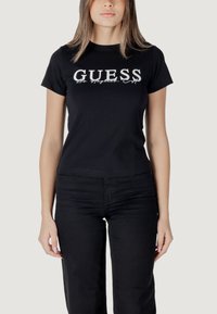 Zwarte katoen t-shirt met het "GUESS" logo in het wit over de borst, ronde halslijn en korte mouwen. Gecombineerd met zwarte broek.