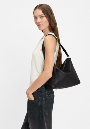 Czarna skórzana torba na ramię o trójkątnym kształcie, gładkiej fakturze i regulowanym pasku. Posiada zamek błyskawiczny oraz subtelne detale w postaci przeszyć.