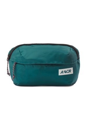 Türkisfarbene rechteckige Reißverschlusstasche mit schwarzem Besatz und doppelten Kordel-Reißverschlussanhängern, vorne mit einem weißen Etikett mit dem "AEVOR"-Logo.