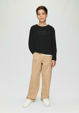 Zwart shirt met lange mouwen met "CODE" opdruk, beige wijde broek, en witte sneakers. Eenvoudig ontwerp, neutrale kleuren en relaxte pasvorm.