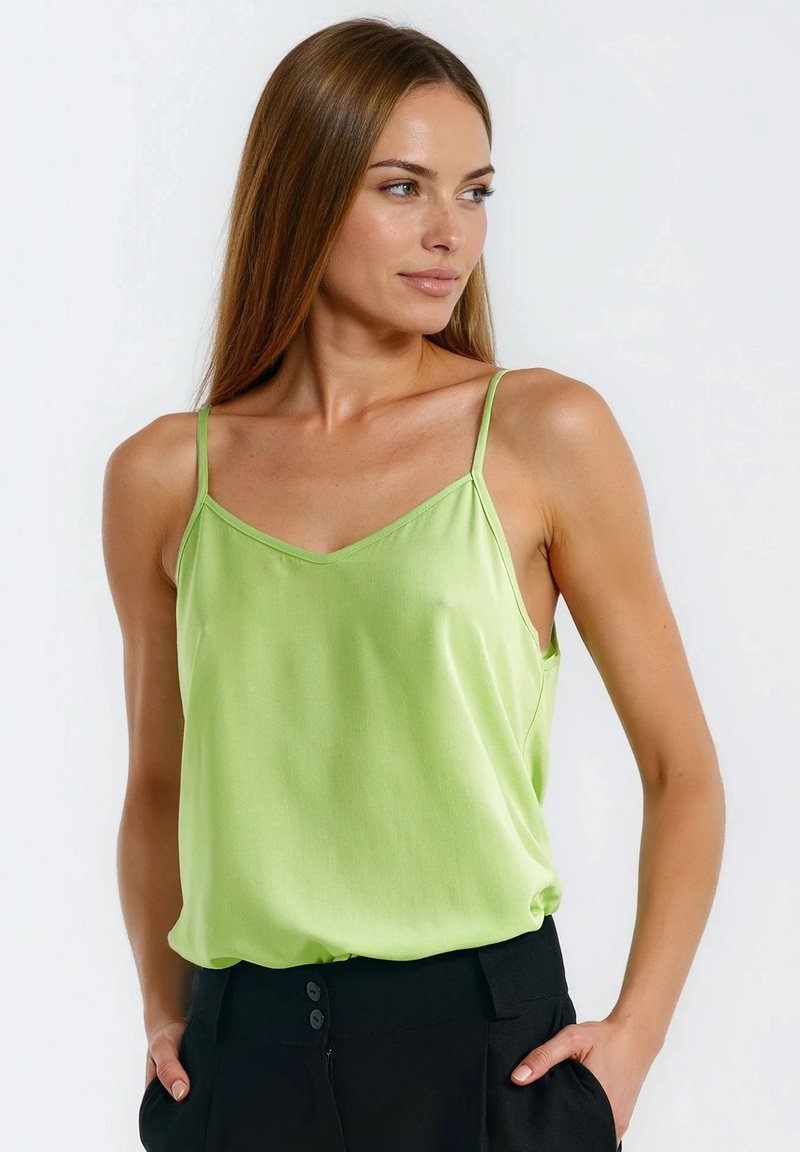 Zielona satynowa koszulka na cienkich ramiączkach, z dekoltem w kształcie litery V i luźnym krojem, zestawiona z czarnymi, wysokim stanem spodniami. Gładka faktura i jasny kolor.
