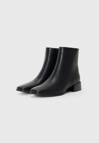 Botas de tobillo de cuero negro con un acabado suave, punta redondeada y estilizada, y un tacón cuadrado bajo. Presentan un diseño minimalista y sin herrajes visibles.
