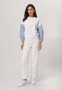 Vit sweatshirt med randiga blå långa ärmar, matchad med högmidjade vita byxor och vita sneakers. Mjuk tyg, avslappnad design.