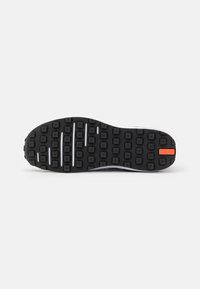 Fekete sneaker talp téglalap alakú tapadási mintával, hangsúlyos barázdákkal és narancssárga díszítéssel. Texturált gumi a tapadás és tartósság érdekében.