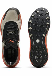 Le sneakers Puma presentano una parte superiore nera e grigia, mesh testurato e una suola nera robusta con accenti arancioni e modelli di battistrada grigi.