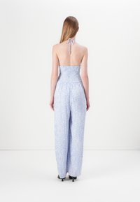 Blå blomstermønster jumpsuit med smocket bodice, vide ben og halterneck-knute. Materialet ser lett ut med en myk tekstur.