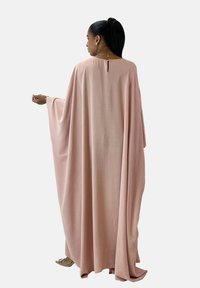 Long, flowing kaftan in soft pink fabric with a loose fit, featuring wide sleeves and a back keyhole detail. Smooth, lightweight texture.