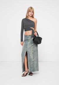 Šedý crop top s dlhým rukávom a asymetrickým výstrihom, doplnený o džínovú maxi sukňu s hadím vzorom a vysokým rozparkom, spolu s čiernymi sandálmi na podpätku so šnúrkami.