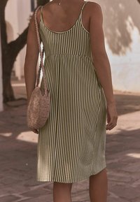 Gestreiftes olivgrünes Kleid mit tailliertem Oberteil und ausgestellt Rock, dünnen Trägern und einer strukturierten, gewebten Handtasche mit Schulterriemen.