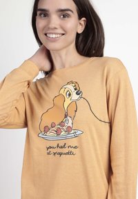 Camiseta amarilla de manga larga con un perro de dibujos animados sosteniendo espaguetis y albóndigas, con el lema "me tuviste con espaguetis". Textura suave, corte relajado.