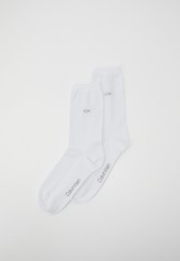 Balti medvilniniai pėdkelnių kojinės su raukšlėmis, turinčios pilką siuvinėtą "CK" logotipą ir "Calvin Klein" tekstą. Lygus paviršius, standartinio dydžio.