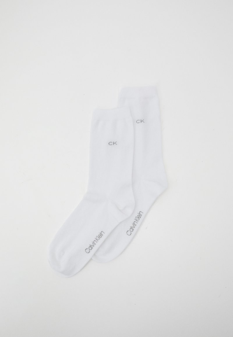 White cotton crew socks with ribbed cuffs, featuring a gray embroidered "CK" logo and "Calvin Klein" text. Smooth texture, standard fit.