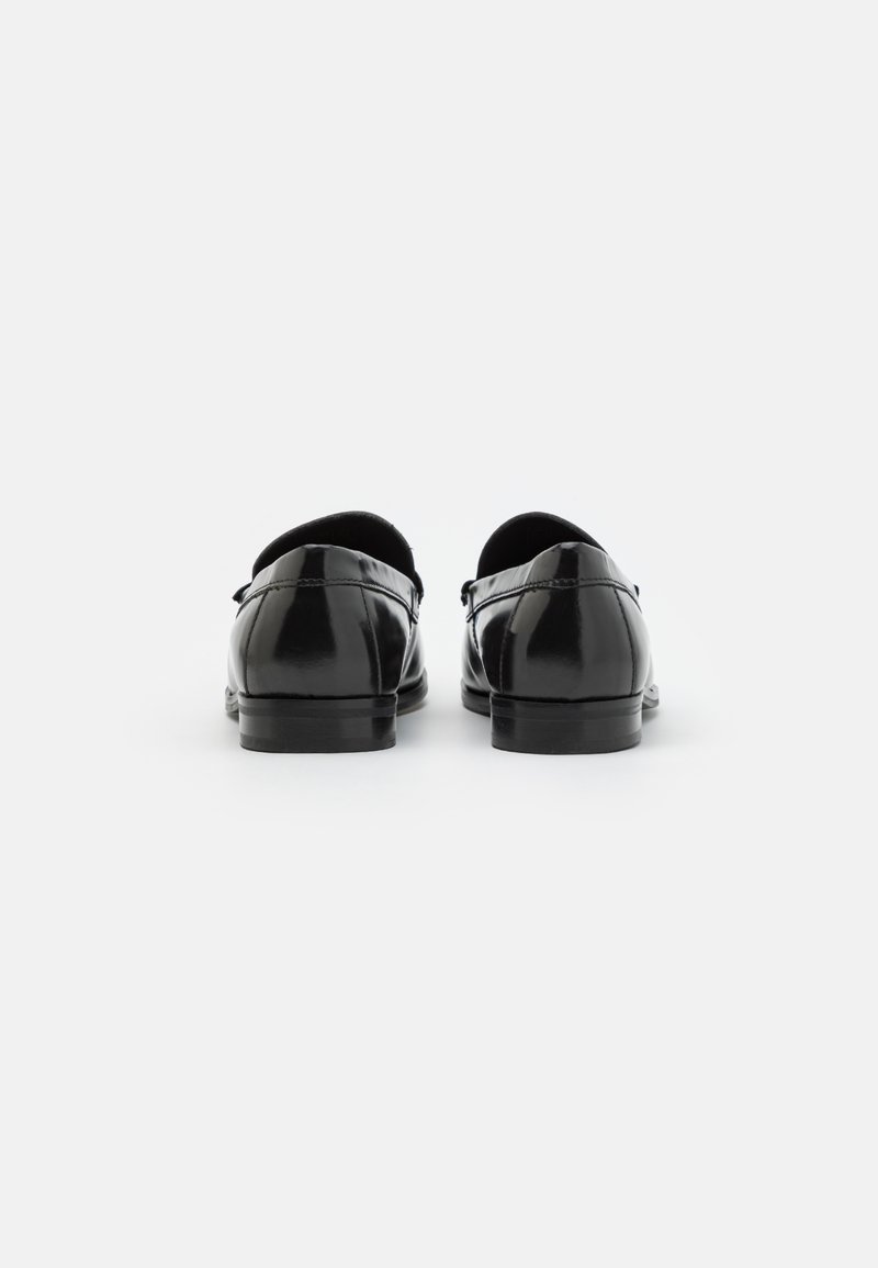 Mocasines de charol negro con forro suave, punta redondeada, tacón bajo y detalles de costura. Textura lisa y diseño minimalista.