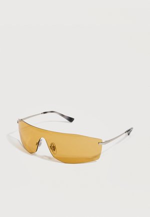 Gafas de sol tipo escudo con tintado amarillo, varillas delgadas de metal plateado y puntas negras curvadas sobre fondo blanco.