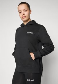 Svart hoodie av mjukt material, med en framficka, sidoflikar och vit "adidas"-logotyp på bröstet.