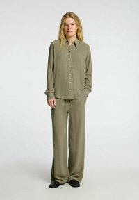 Olijfgroene shirt met een knoopsluiting aan de voorkant en lange mouwen, gecombineerd met bijpassende losse broek, gemaakt van lichtgewicht stof.