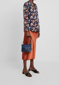 Blusa floreale blu navy con maniche lunghe, fiori arancioni e bianchi; gonna midi in raso color ruggine; borsa in pelle sintetica blu navy con texture coccodrillo; sandali con tacco a blocco neri.