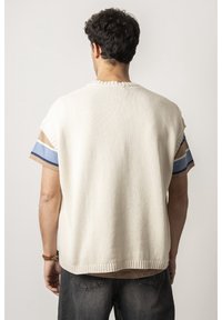 Herren-Pullover mit kurzen Ärmeln in Creme mit geripptem Saum. Hergestellt aus strukturiertem Stoff und mit gestreiften hellblauen und braunen Akzenten an den Schultern.