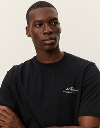 Čierne bavlnené tričko s okrúhlym výstrihom, na ľavej strane hrudníka s bielym textom "Les Deux International Sporting Goods Established in 2011."