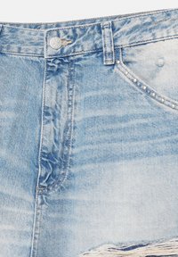 Svetlo modra denim krilo z gumbi spredaj, zadrgo, zankami za pas in srebrnimi zakovice ob desnem robu žepa.