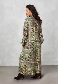 Vestido largo y estampado que presenta diseños geométricos en verde, beige y negro. La tela parece ligera, con mangas largas y un corte relajado.
