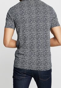 Polo tričko s krátkým rukávem v navy modré barvě s bílým květinovým vzorem. Bavlněný materiál, přiléhavý střih, žebrovaný límec a detaily na zadní straně.