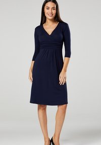 Navy wrap dress with three-quarter sleeves, textured bust, and a flared skirt. Made from soft, stretchy fabric for a comfortable fit.