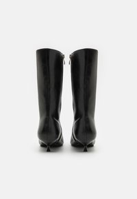 Bottes noires en cuir montantes avec un design épuré, bout pointu et talon étroit. Présentent une fermeture éclair à l'arrière.