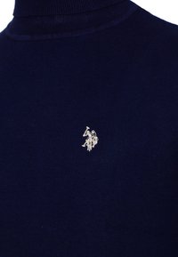 Suéter de cuello alto azul oscuro con un pequeño logotipo de jugador de polo bordado en color claro en el pecho.