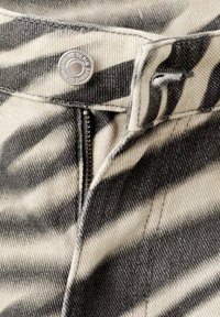 Gros plan sur un jean en jean à motif zèbre avec une fermeture éclair partiellement ouverte et un bouton argenté marqué "Spring Denim".