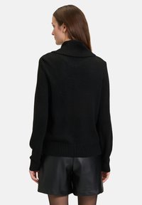 Zwarte gebreide trui met een hoge ribbels kraag, ingezakte schouders en ribbelzoom, gecombineerd met zwarte leren shorts, met een gladde textuur.