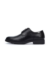 Chaussure habillée en cuir noir avec une finition lisse, bout arrondi, design à lacets avec six œillets, et un talon bas empilé. Étiquette de marque notable sur le côté.