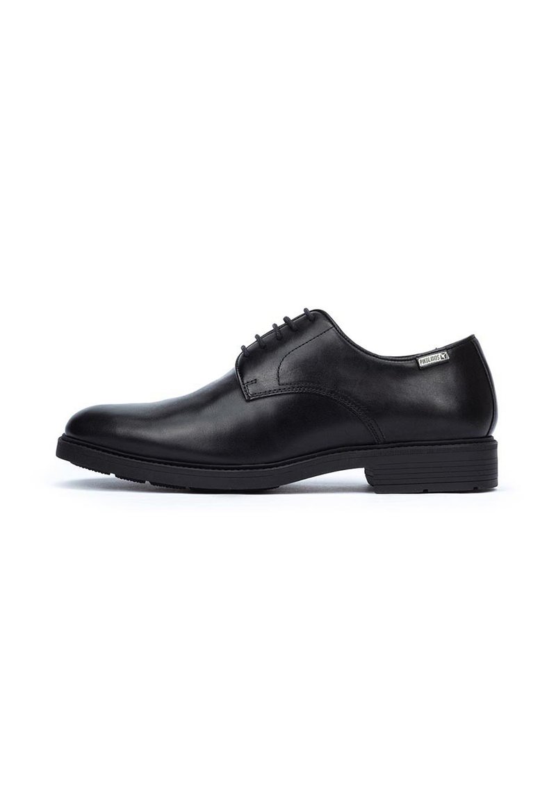Chaussure habillée en cuir noir avec une finition lisse, bout arrondi, design à lacets avec six œillets, et un talon bas empilé. Étiquette de marque notable sur le côté.