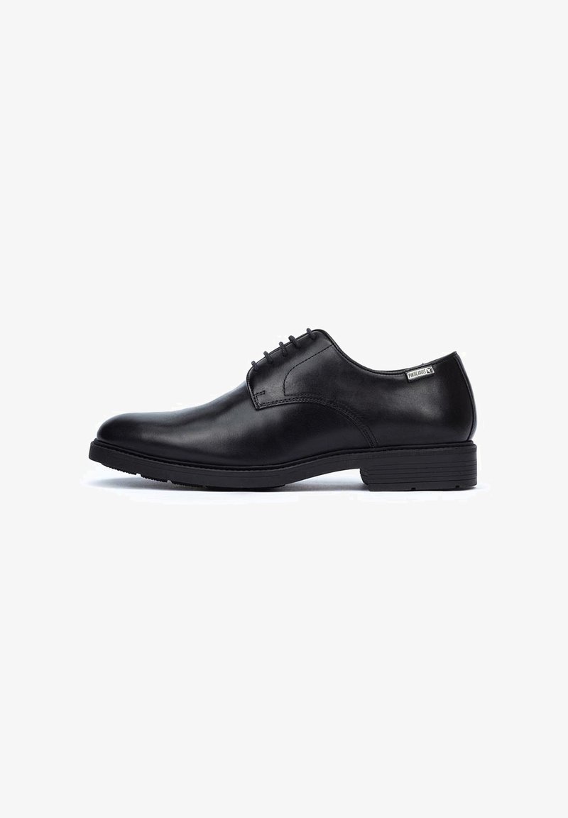 Chaussure habillée en cuir noir avec une finition lisse, bout arrondi, design à lacets avec six œillets, et un talon bas empilé. Étiquette de marque notable sur le côté.