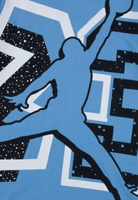 Blue T-shirt featuring a black silhouette of a jumping figure, surrounded by white and black geometric patterns with a speckled background.