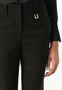 A fekete szabott nadrág sima anyagból készült, karcsúsított szabású, és fémcsattal díszített derékpánttal rendelkezik a kifinomult megjelenés érdekében.