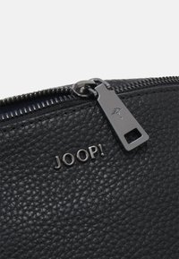 Black textured leather bag featuring a silver logo "JOOP!" and a sleek zipper pull with a decorative emblem.