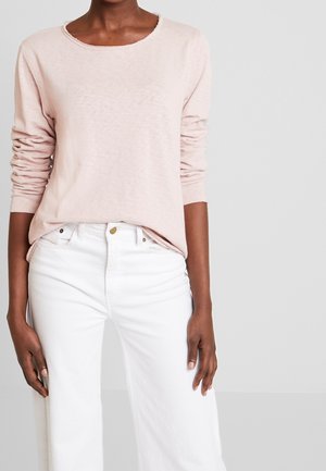 Helles rosa Langarmoberteil aus weichem Stoff mit Rundhalsausschnitt, kombiniert mit weißen hoch taillierten Jeans mit Fronttaschen und Knopfdetails.