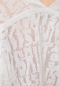 Leichtes, cremfarbenes Strickoberteil mit offener Webstruktur, V-Ausschnitt und strukturierten Garnakzenten mit geometrischen Motiven.