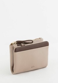 Portefeuille en cuir beige avec un accent supérieur marron, doté d'une fermeture éclair, d'une dragonne et d'une surface texturée. Forme rectangulaire compacte.