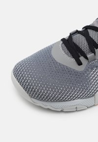 Grå atletiska skor med en texturerad stickad överdel, mesh-accenter och svarta snörningar. Har en vadderad ankel och en lätt gummisula.