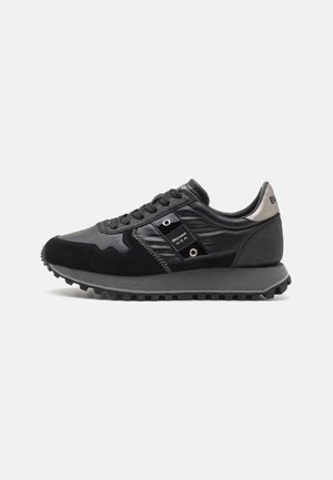 Sneaker preto com uma mistura de camurça e materiais sintéticos brilhantes. Apresenta superfícies texturizadas, costuras proeminentes e uma sola de borracha com aderência.