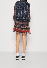 Mörkblå blommig klänning med genomskinliga långa ärmar, lagerdesign och mönstrad nederkant med röda accenter. Kombination med vita strumpor och marinblå skor.