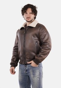 Giacca bomber in pelle marrone con colletto in shearling crema, chiusura a zip e polsini a costine. Presenta tasche laterali e una superficie liscia.
