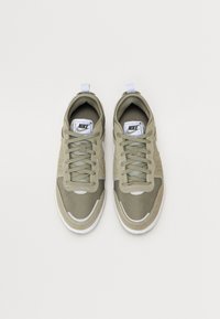 Sapatilhas Nike verde claro com parte superior em malha, bico arredondado, detalhes em branco e textura. Apresenta atacadores e uma alça na parte de trás.
