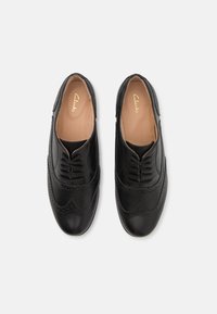 Chaussures à lacets en cuir noir avec un design brogue comportant des perforations décoratives et une texture lisse. Intérieur avec une doublure beige clair.